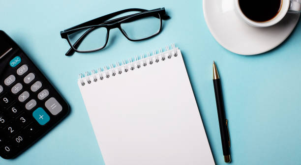 istock Glasses, calculator, blank notebook and pen on a light blue background. Copy space 1294325582