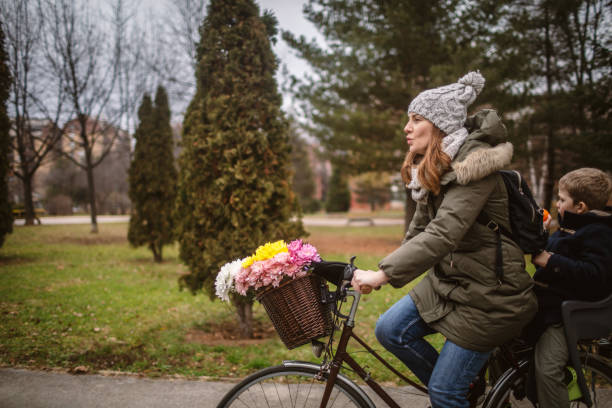 Photo of woman and her son are riding the bicycle in a public park.Mother ride her boy home after kindergarten time.