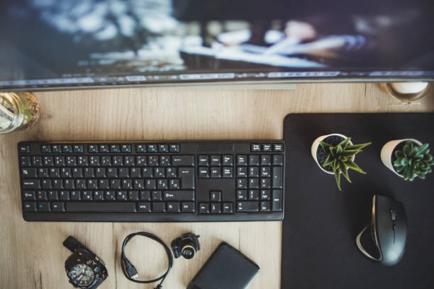 Top view of a wooden surface with keyboard, mouse, monitor, external hard dist, clock and usb cables
