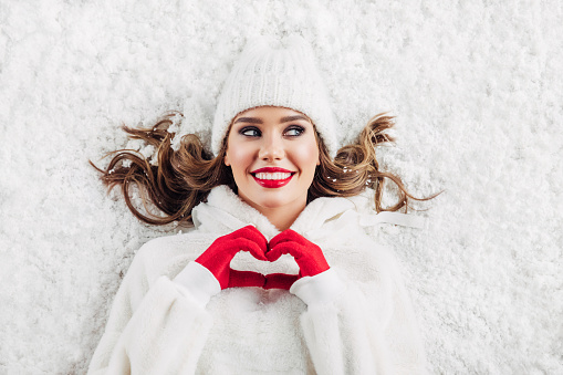 Girl lying down on the snow showing love sign