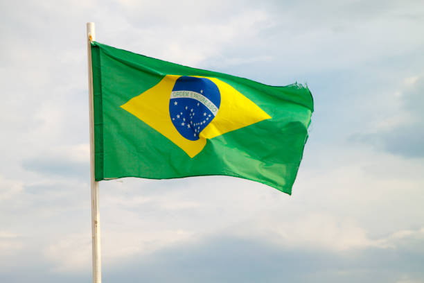 istock Brazilian flag on a blue sky with clouds background 1294335626