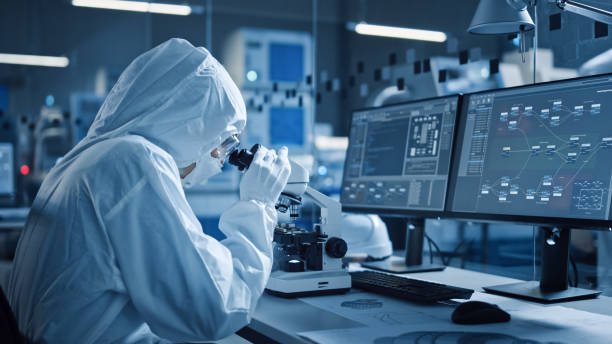 istock Research Factory Cleanroom: Engineer or Scientist in Coveralls Works on Computers, Uses Microscope to Inspect Motherboard Microprocessor, Developing Electronics for Medical Electronics 1294339607