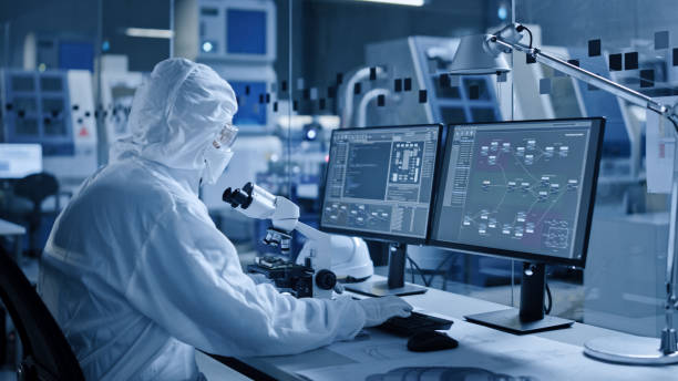 istock Electronics Factory Cleanroom: Engineer / Scientist in Coveralls Works on Computer, Screen Shows Infographics and Software System Control UI, Developing Electronics for Medical Electronics 1294339631