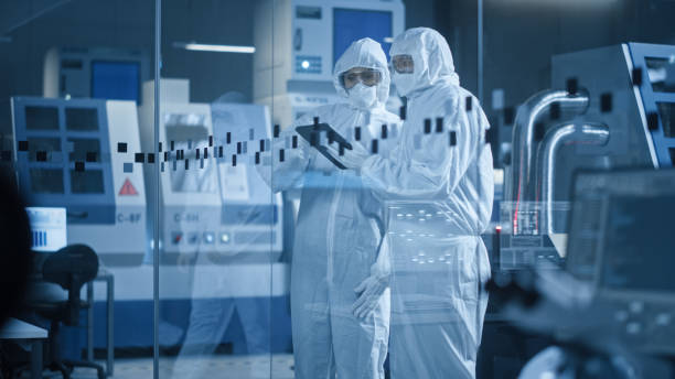 istock Factory Cleanroom: Engineer and Scientist Wearing Coveralls, Standing in Workshop Talk and Use Tablet Computer, Professionals Develop Technology for Modern CNC Machinery and Electronic Equipment 1294339633