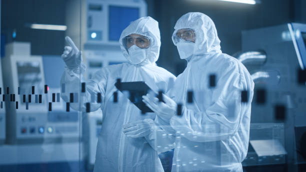 istock Factory Cleanroom: Engineer and Scientist Wearing Coveralls, Standing in Workshop Talk and Use Tablet Computer, Professionals Develop Technology for Modern CNC Machinery and Electronic Equipment 1294339646