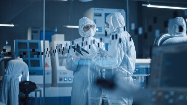 istock Factory Cleanroom: Engineer and Scientist Wearing Coveralls, Standing in Workshop Talk and Use Tablet Computer, Professionals Develop Technology for Modern CNC Machinery and Electronic Equipment 1294339654