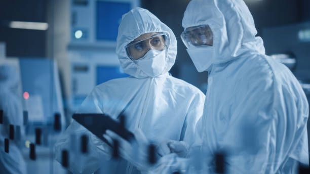 istock Factory Cleanroom: Engineer and Scientist Wearing Coveralls, Standing in Workshop Talk and Use Tablet Computer, Professionals Develop Technology for Modern CNC Machinery and Electronic Equipment 1294339667