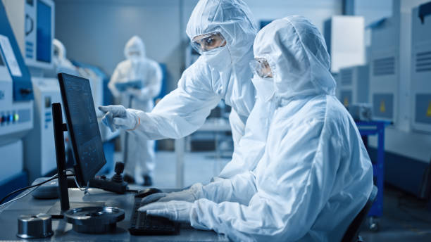 sala limpia de fábrica: ingeniero y científico que llevan coveralls y máscaras tienen discusión, utilice la computadora mostrando el control del sistema de infraestructura. en maquinaria cnc de fondo, equipos electrónicos - work wear factory people occupation fotografías e imágenes de stock