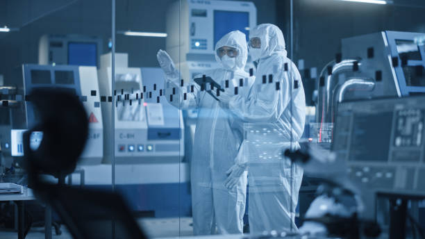 Factory Cleanroom: Engineer and Scientist Wearing Coveralls, Standing in Workshop Talk and Use Tablet Computer, Professionals Develop Technology for Modern CNC Machinery and Electronic Equipment