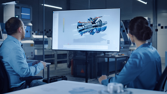 Office Meeting: Confident Female Engineer Talks to Project Manager, Watching Interactive Digital Whiteboard TV that Shows New Sustainable Eco-Friendly Engine 3D Concept. Modern Factory with Machinery