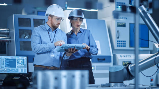 istock Factory Workshop: Professional Female Engineer, Male Machinery Operator Use Industrial Digital Tablet Computer to Work and Program Robot Arm for Production Line. High-Tech Facility with CNC Machines 1294339692