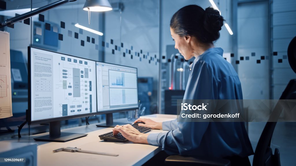 Factory Office: Portrait of Beautiful and Confident Female Industrial Engineer Working on Computer, on Screen Industrial Electronics Design Software. High Tech Facility with CNC Machinery Computer Software Stock Photo