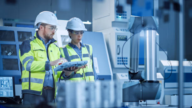 istock Factory Workshop: Professional Female Engineer, Male Machinery Operator Use Industrial Digital Tablet Computer to Work and Program Robot Arm for Production Line. High-Tech Facility with CNC Machines 1294339709