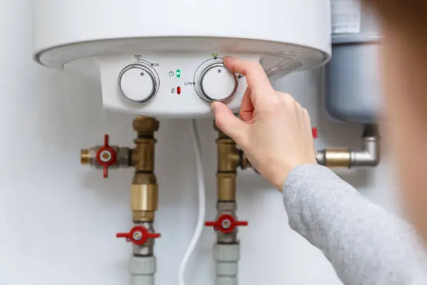 Photo of Female hand puts thermostat of electric water heater (boiler) in economy mode.