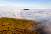 Aerial view of mountains rising through a sea of clouds (Skirrid Fawr, Wales, UK)