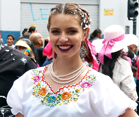 Cuenca, Ecuador - February 22, 2020: Carnival parade in Cuenca city. Beautiful woman dancer in embroidered blouse with typical design for Ecuador smiling to audience. Foam is spraying at everyone
