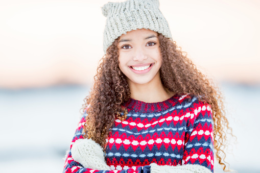 A portrait of a beautiful mixed race teenager enjoying her time outside during winter time. She wears warm clothing and a winter hat.