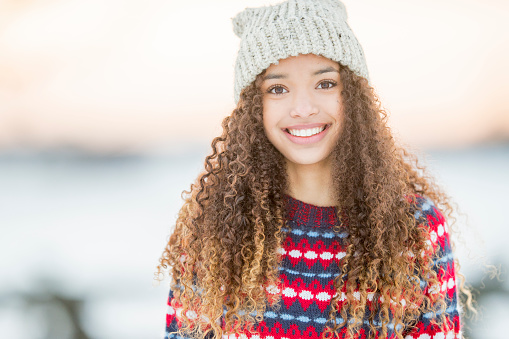 A portrait of a beautiful mixed race teenager enjoying her time outside during winter time. She wears warm clothing and a winter hat.