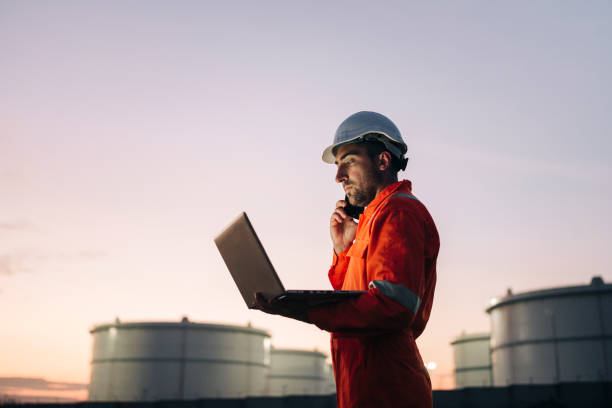 Engineer using laptop near oil refinery at night stock photo