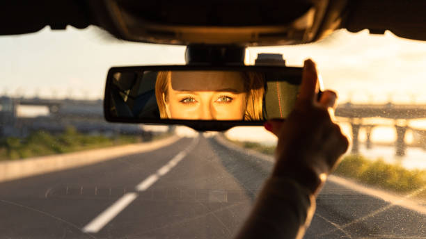 istock Cheerful joyful woman adjusting mirror while sitting in her car, looking in reflection at camera. Sunset time 1294350872