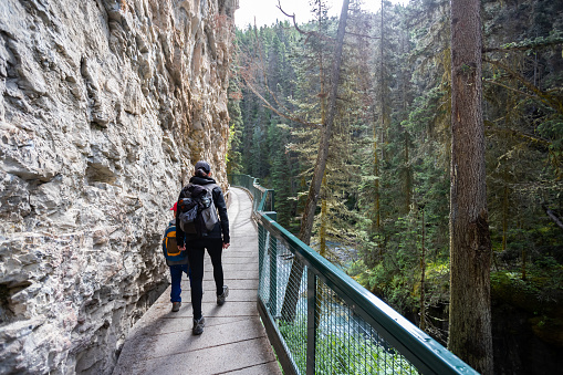 Mother and Son Hiking at Johnson Canyon in Banff National Park, Canada. They are holding hands and bonding as they are walking on the bridge and footpath.