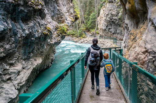 Mother and Son Hiking at Johnson Canyon in Banff National Park, Canada. They are holding hands and bonding as they are walking on the bridge and footpath.