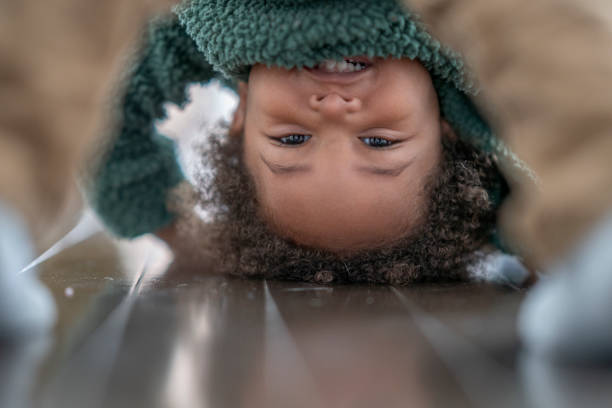 An adorable little boy bends down over and looks directly into the camera. He is in a very playful mood.
