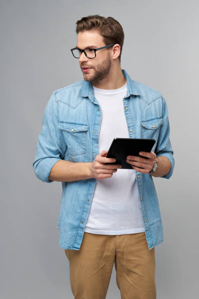istock Happy young man wearing jeans shirt standing and using tablet over studio grey background 1294358110