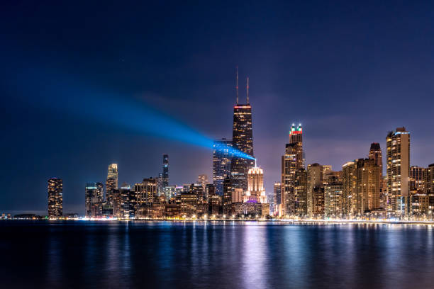 Downtown Chicago Skyline at Night Chicago cityscape at night with Lindbergh Beacon shining light on Lake Michigan chicago illinois stock pictures, royalty-free photos & images