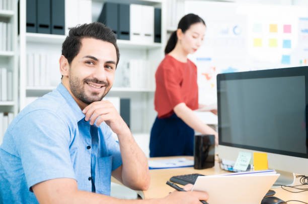 istock Young asian man working on a computer at workplace. He looked straight at the camera and smile 1294377763