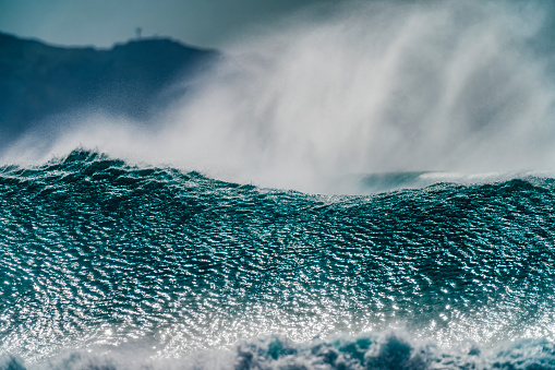 Wave rocks crashing exploding white ocean sea water spray power into blue sky along rocky coastline close-up Photograph.