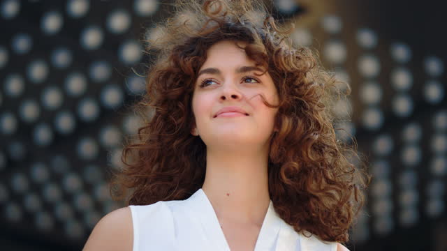 Curly girl looking into distance outdoors. Fashion model smiling outside.