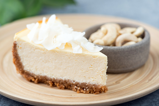 Vegan cashew cheesecake with coconut flakes served on a bamboo plate