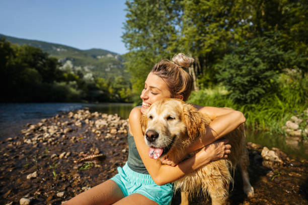 Days like this Photo of a smiling young woman and her dog enjoying the beautiful, warm summer afternoon by the river, far from the hustle of the city. dog swimsuit stock pictures, royalty-free photos & images