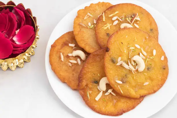 Photo of Creamy Indian Mithai Dessert Mawa Malpua Loaded With Khoya And Ghee And Topped With Nuts Dry Fruits Served In Plate With Rose Petals Decoration. Isolated On White Background With Copy Space For Text