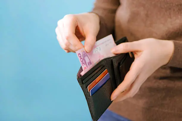 Photo of A woman takes out Ukrainian hryvnia money from a purse on a blue background with a place for the text. payment concept