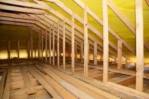 Photo of A close-up on an unfinished attic construction with wooden roof beams, planks, rafters, ceiling joists and vapor barrier film inside a new house.