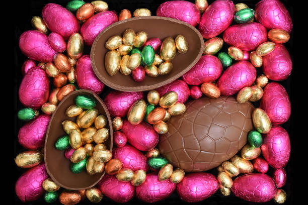 istock Pile or group of multi colored and different sizes of colourful foil wrapped chocolate easter eggs in pink, red, gold and lime green with two halves of a large brown milk chocolate egg in the middle and mini eggs inside. 1294400190