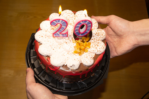 in someone's hands is a round cake with candles in the form of a figure of twenty. Birthday.