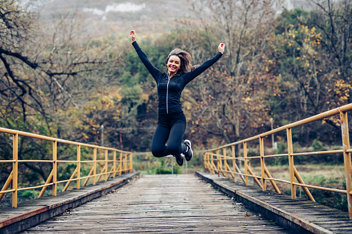 Full length shot of a happy young woman jumping into the air against a gray background.