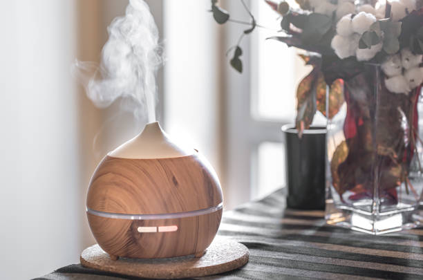 Modern oil aroma diffuser in the living room on the table. Composition with air humidifier and flowers in a vase. Health care concept. home diffuser stock pictures, royalty-free photos & images