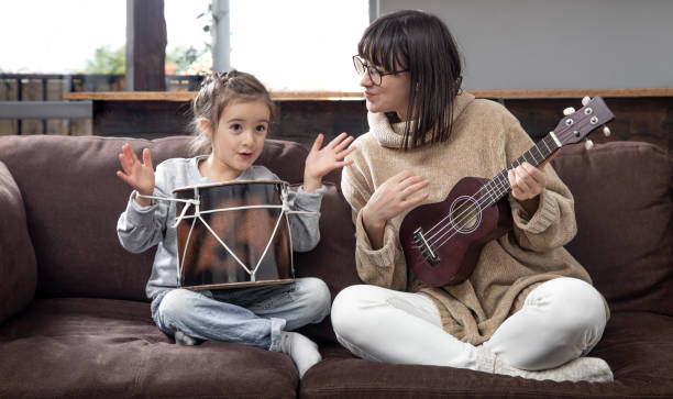 młoda matka i córka grają na instrumentach muzycznych w domu. - 20s acoustic guitar adult art zdjęcia i obrazy z banku zdjęć