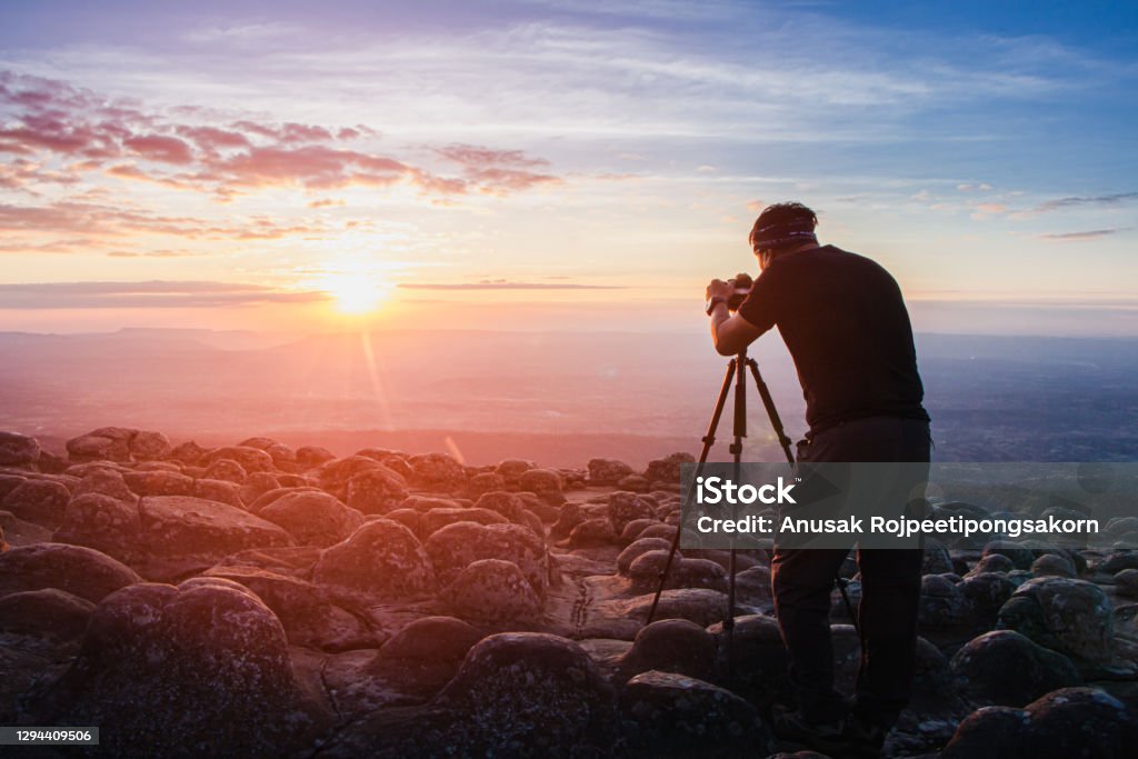 man photographer holding a camera to shoot nature sunrise at mountain scenery.Tourists take pictures of sunset nature with camera on a tripod with copyspace. Photographer Stock Photo
