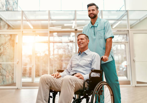 Doctor team. Medicine. A young handsome doctor with his elderly disabled person in a wheelchair walk the corridors of a modern clinic. demobilization photos stock pictures, royalty-free photos & images