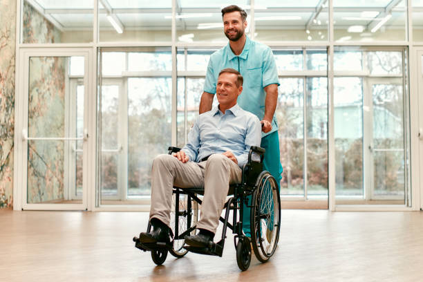 Doctor team. Medicine. A young handsome doctor with his elderly disabled person in a wheelchair walk the corridors of a modern clinic. demobilization photos stock pictures, royalty-free photos & images