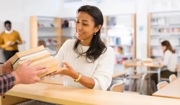 Portrait of young adult woman returning books to librarian at public library