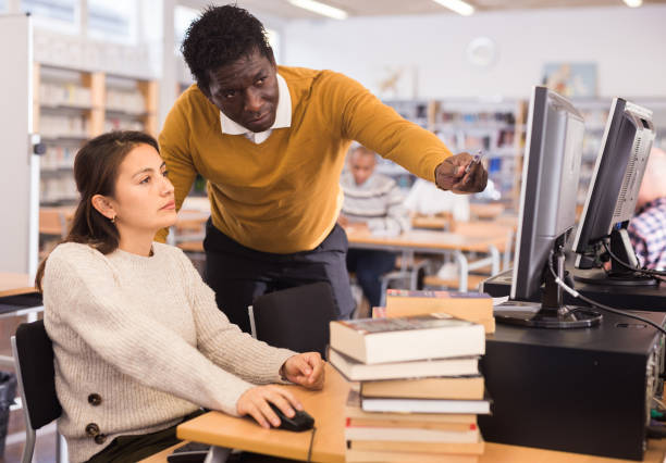 Portrait of librarian assisting woman in library Portrait of confident man librarian assisting woman in library librarian stock pictures, royalty-free photos & images