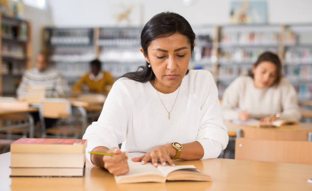 istock Concentrated hispanic woman reading books in public library 1294410090