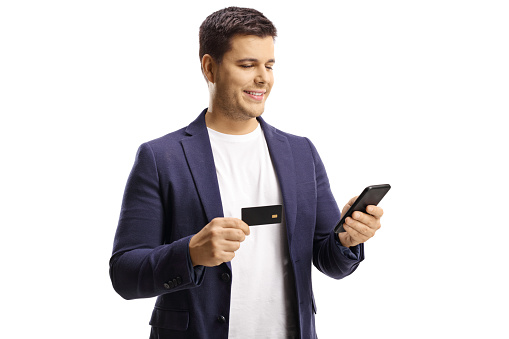 Young man holding a credit card and using a mobile phone isolated on white background