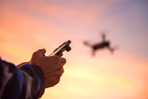 Man operating a drone with remote control in sunset.